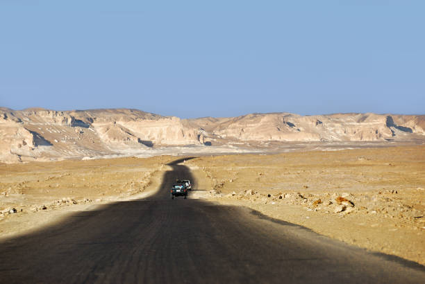 Tar road along sand dunes and sandstone rocks in Western desert between Farafra and Bahariya oasis. Sahara desert, Egypt, Africa. Selective focus on the car